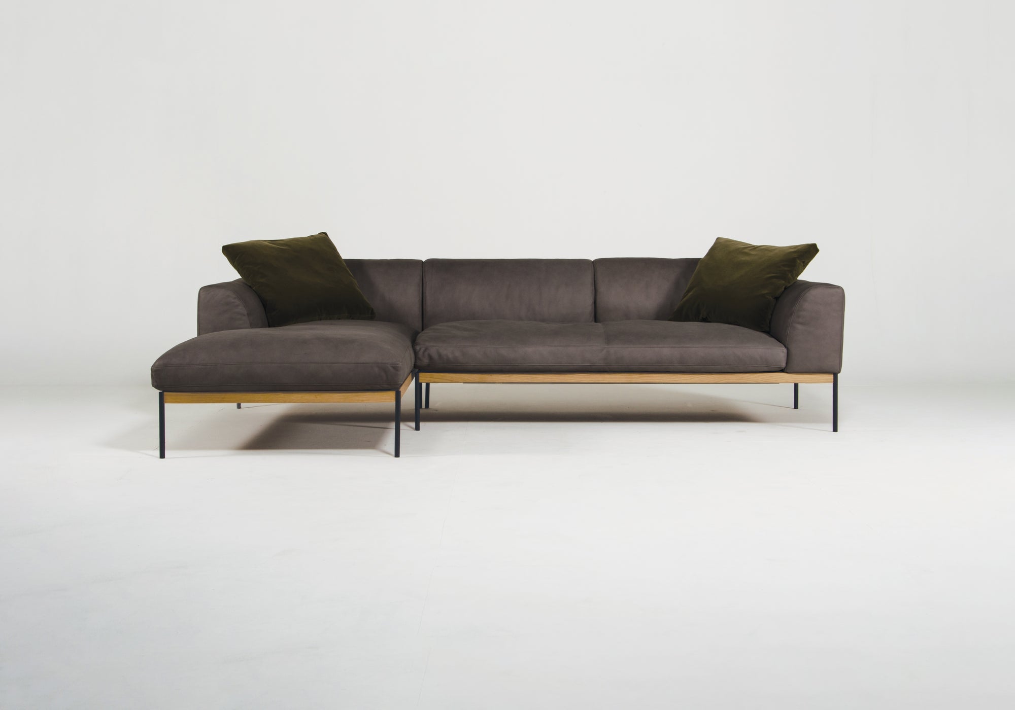 The Wooden Stories Department Modular Sofa | Leather • M2 Left features dark gray upholstery, black metal legs, a solid wood base, wooden frame accents, and includes two dark green pillows, shown against a plain white background.