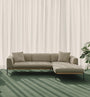 The Department Modular Sofa | Fabric • M2 Right by Wooden Stories in beige sits on a green carpet before sheer white curtains, sunlight casting shadows nearby, while a leafy potted plant stands beside its solid wood Danish-inspired base.