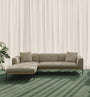 The Wooden Stories Department Modular Sofa | Fabric • M2 Left in beige, with two cushions, rests on a green carpet near sheer white curtains. Sunlight filters in, casting soft shadows, while a leafy plant stands beside its solid wood base.