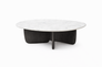 The Eden Coffee Table by Wooden Stories features a round Carrara marble top and a black solid American oak base with curved, intersecting panels—a modern piece embodying Scandinavian simplicity.