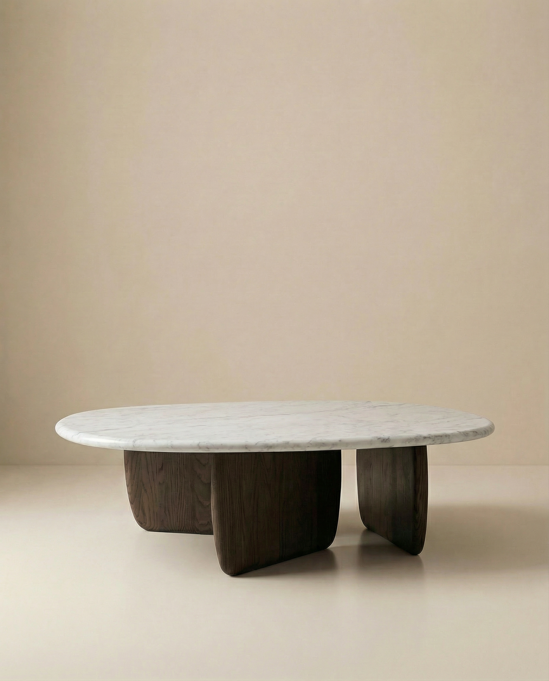 The Eden Coffee Table by Wooden Stories features a smooth oval Carrara marble top and three dark, rounded solid American oak supports, set against a neutral beige background.