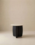 The Eden Side Table | Stone Top by Wooden Stories features a modern round beige stone top and a dark, curved solid American oak base, shown against a plain light beige background.