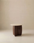 The Eden Side Table | Stone Top by Wooden Stories features a minimalist, modern design with a light stone top and sculptural dark wood base, highlighting Scandinavian simplicity against a plain beige background.
