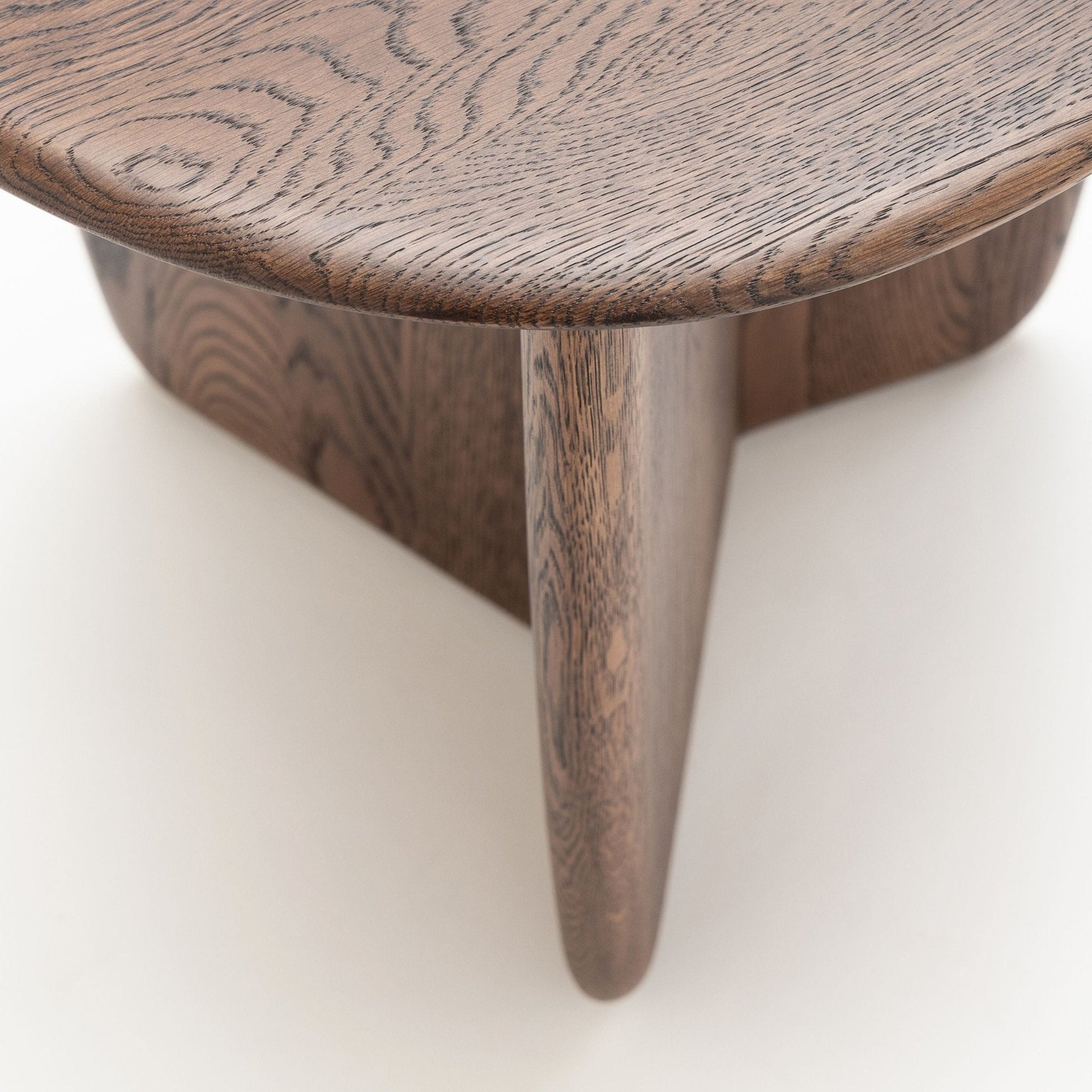 Close-up of the Wooden Stories Eden Side Table, a Scandinavian-inspired piece with smooth, rounded edges, intersecting legs, and natural wood grain set against a light-colored background.