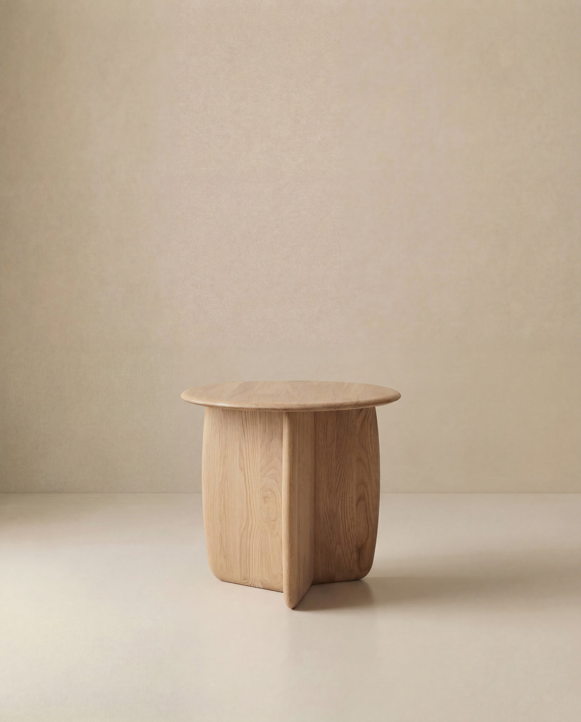 The Eden Side Table by Wooden Stories features a small, round solid wood top and a sculptural base, standing alone against a beige background—ideal for fans of Scandinavian design.