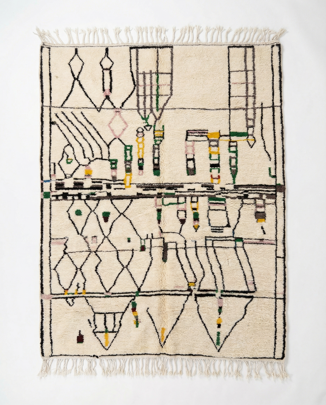 The Jo Moroccan Rug by SOBU is a cream-colored, handwoven wool rug with fringed edges. It displays an abstract geometric pattern in black, green, yellow, and brown arranged asymmetrically on the natural surface.