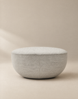 A light gray, oval-shaped Fable Ottoman | Fabric by Wooden Stories from the Danish Collection is displayed on a neutral background with soft lighting, highlighting its smooth, minimalist design.