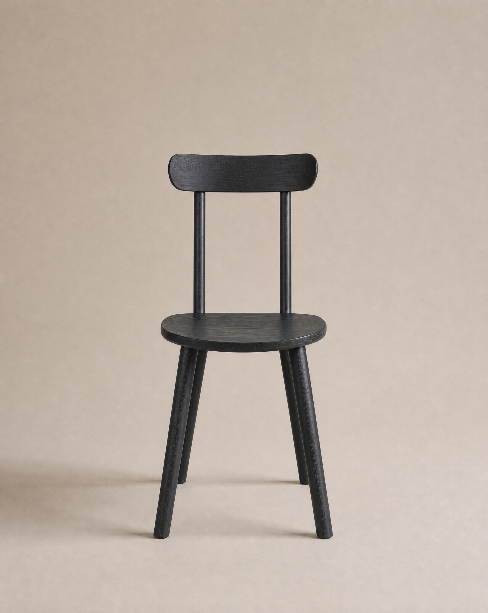 The Figura Dining Chair | Black Oak by Wooden Stories is a sleek, modern Scandinavian piece with four legs, a round seat, and a flat backrest—ideal for contract grade spaces and shown against a plain beige background.