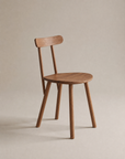 The Figura Dining Chair | Latte Oak by Wooden Stories features a simple wooden design with a round seat, straight legs, and a horizontal backrest, set against a neutral beige background.