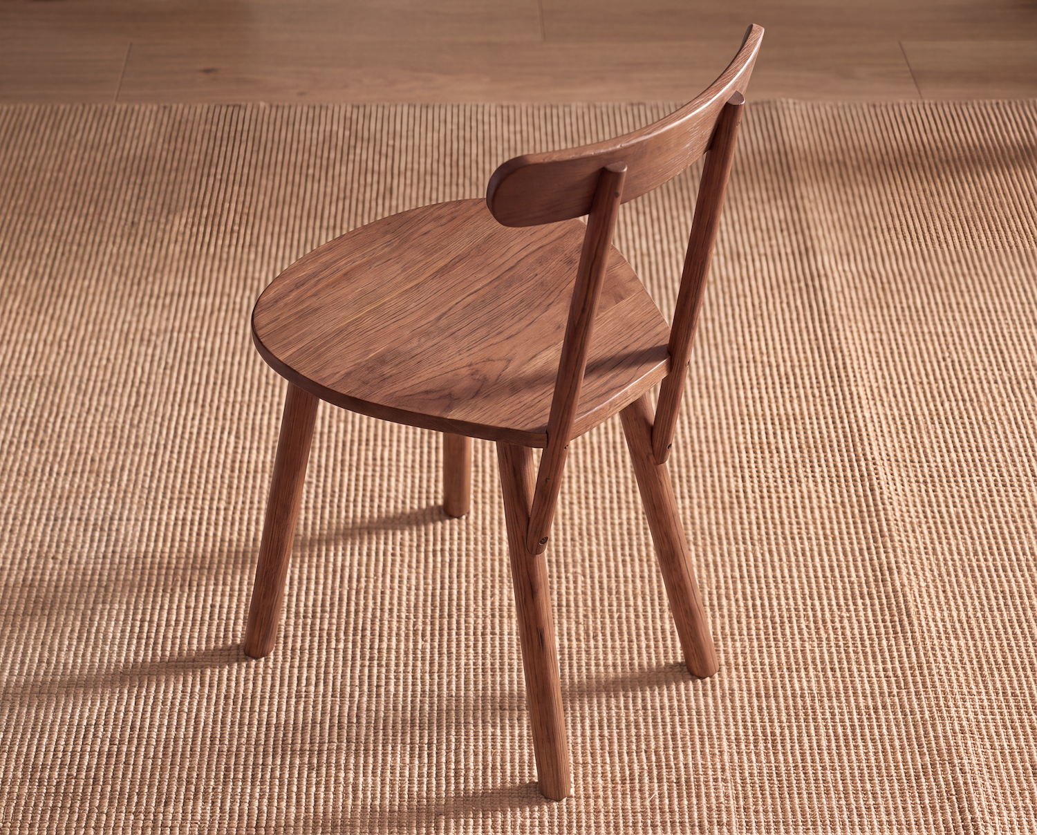 A Figura Dining Chair | Latte Oak by Wooden Stories, featuring a curved backrest and round seat, sits on a woven tan rug. This modern contract-grade dining chair has four legs and showcases a simple, minimalist design. The floor beneath is wood.