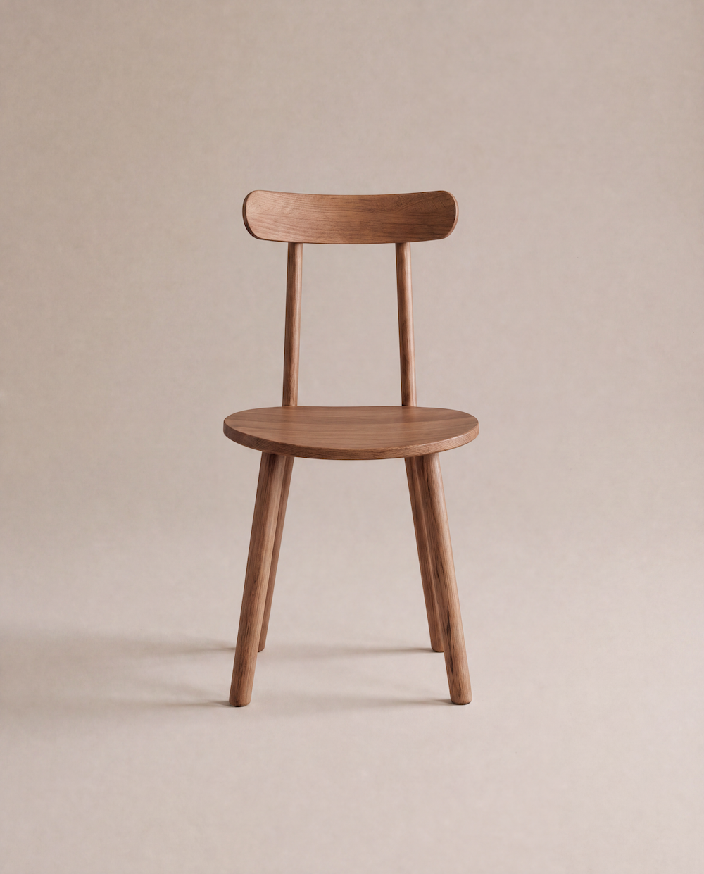 A minimalist Figura Dining Chair | Latte Oak by Wooden Stories, featuring a rounded seat and backrest, four angled legs, and a smooth finish, is displayed against a neutral beige background.