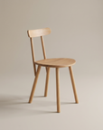 The Figura Dining Chair | Light Oak by Wooden Stories features a simple wooden design with four legs, a round seat, and a straight backrest—showcasing classic Scandinavian style against a light background.