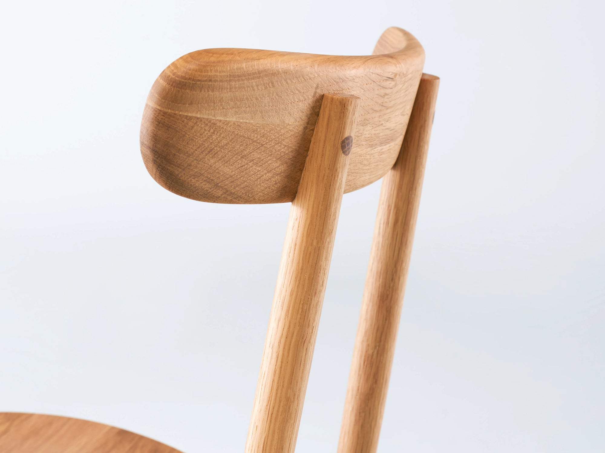 Close-up of the Wooden Stories Figura Dining Chair in Light Oak, featuring a smooth, curved backrest and straight legs—minimalist design with natural wood grain inspired by heritage woodworking, set against a plain white background.