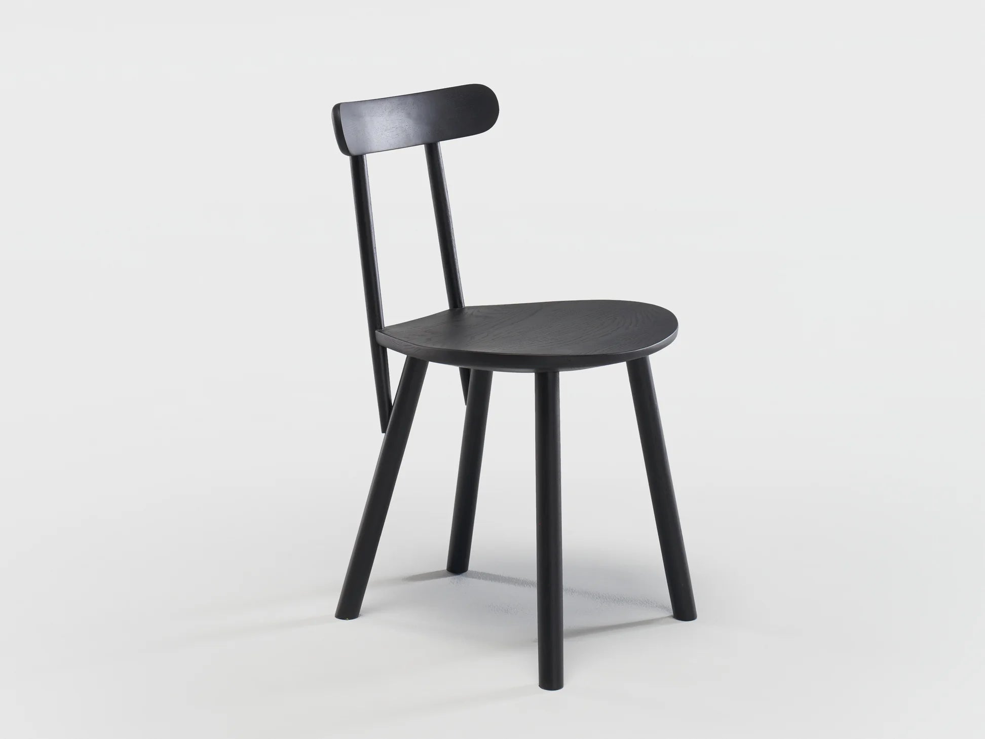 The Figura Dining Chair by Wooden Stories features a minimalist black oak design with three legs, a round seat, and a slim backrest bar, inspired by heritage woodworking, shown against a plain white background.