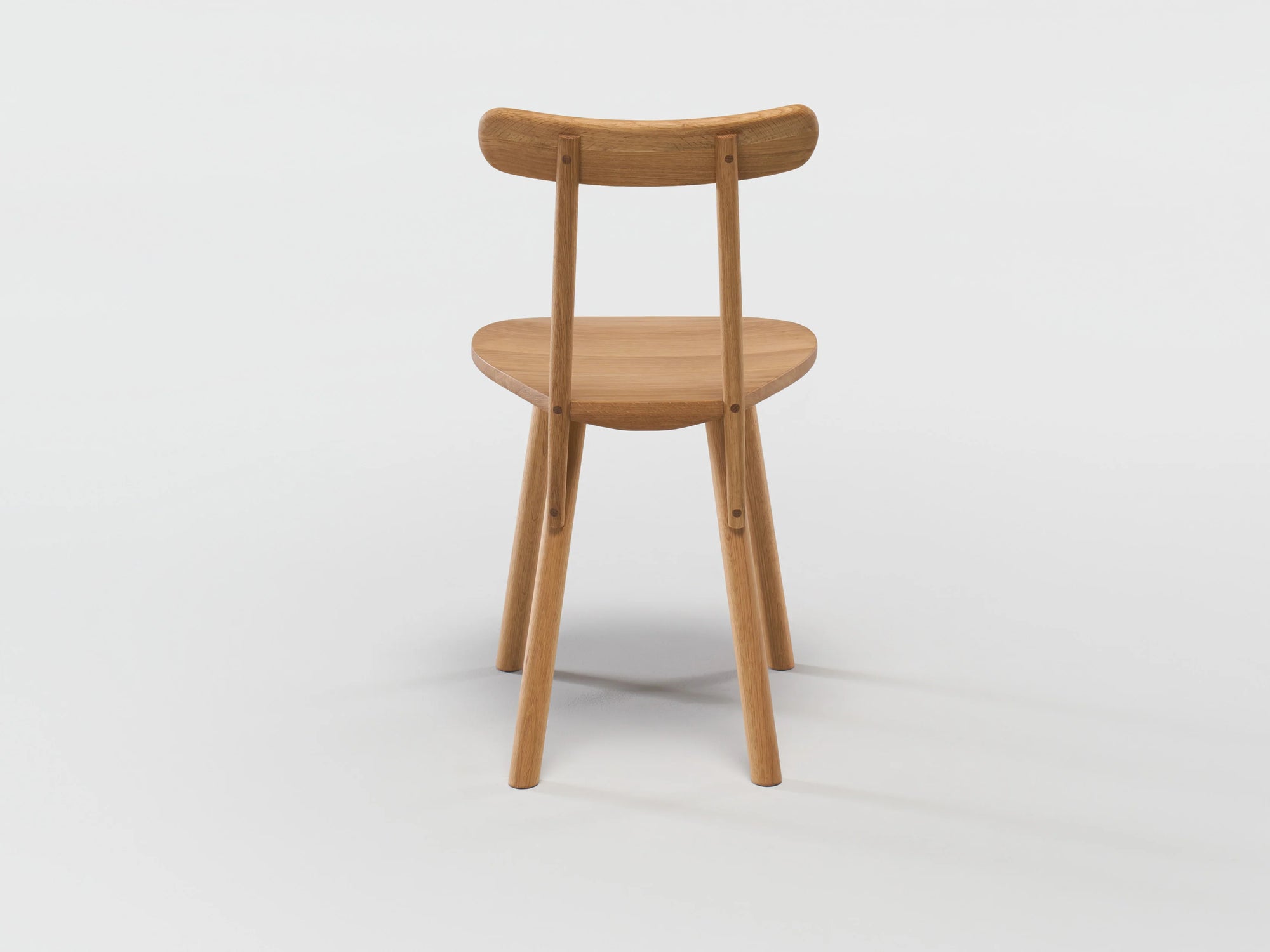 The Figura Dining Chair by Wooden Stories, shown from behind in light oak, features a curved backrest and minimalist silhouette—blending heritage woodworking with modern design against a plain white background.