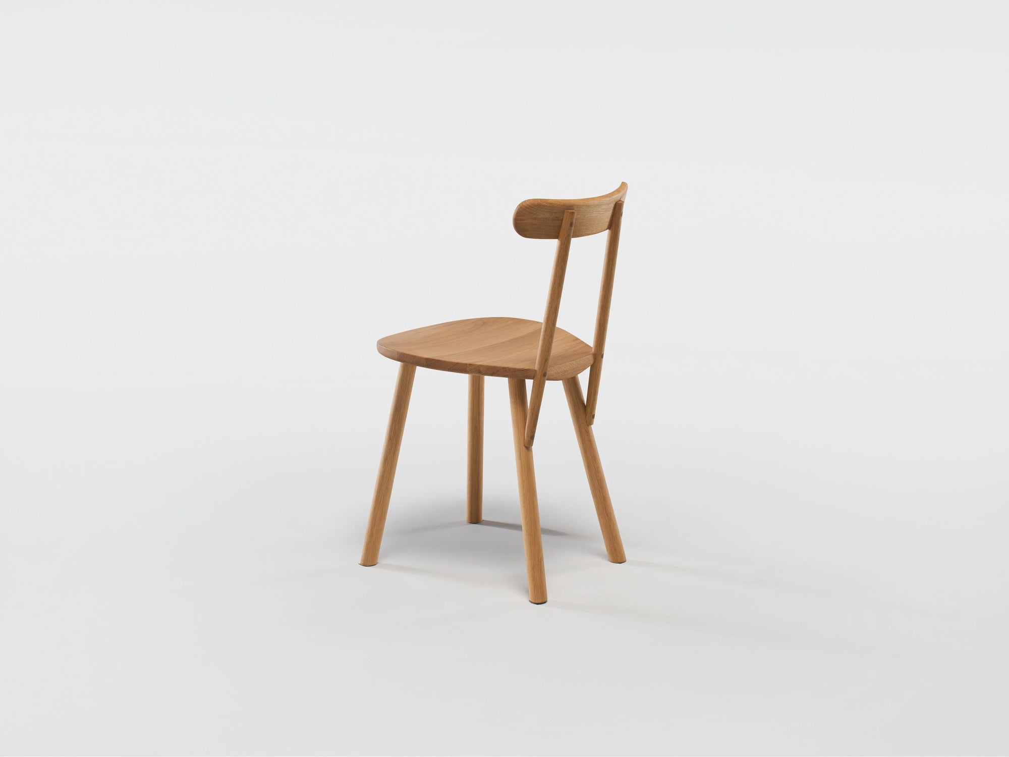 The Figura Dining Chair by Wooden Stories features a minimalist solid light oak design with a curved backrest and angled legs, highlighting heritage woodworking. Shown on a plain white background.