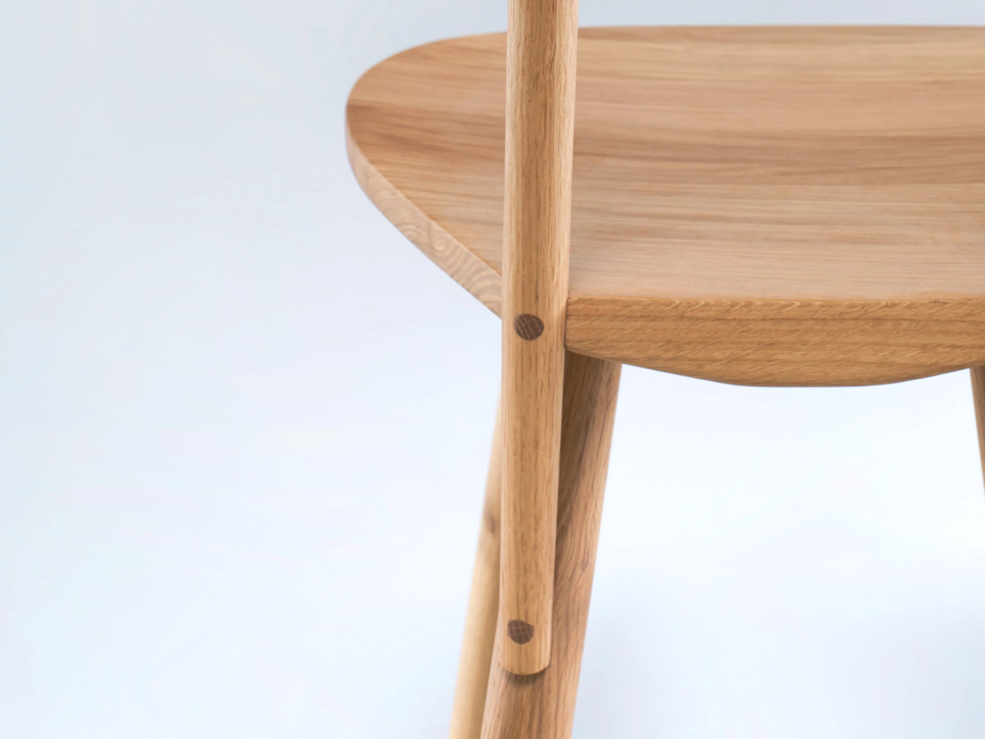 Close-up of the Figura Dining Chair | Light Oak by Wooden Stories, highlighting the smooth curved seat, seamless leg joint, and natural wood grain. Minimalist heritage woodworking design stands out against a plain light background.