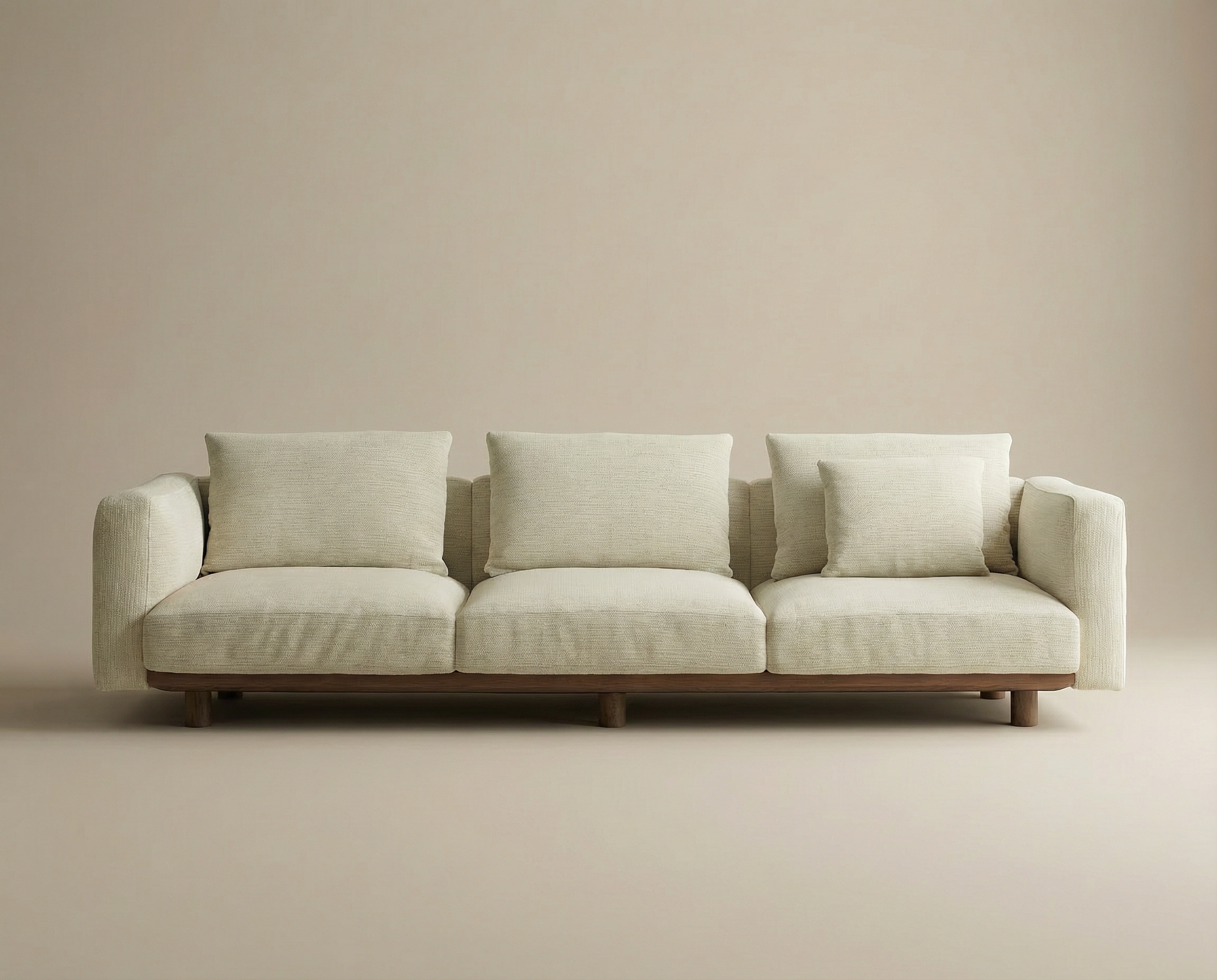 The Islet Sofa | Fabric by Wooden Stories is a modern beige sofa with three seat cushions, four back cushions including a smaller one, set against a plain, light-toned wall and floor background.