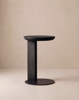 The Guild Side Table by Wooden Stories features a modern black design with a round top and base, connected by a single vertical support, and is showcased against a plain beige background.