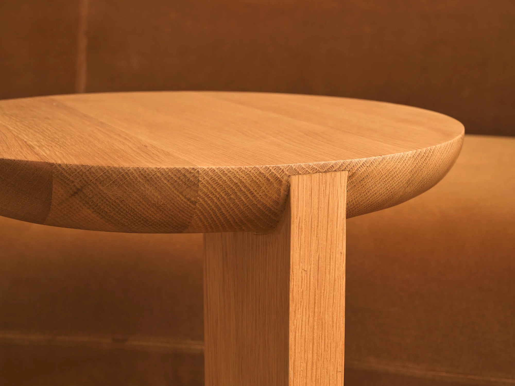 Close-up of the Guild Side Table in Light Oak by Wooden Stories, featuring Danish lines and a smooth, modern finish, set against a brown upholstered background.