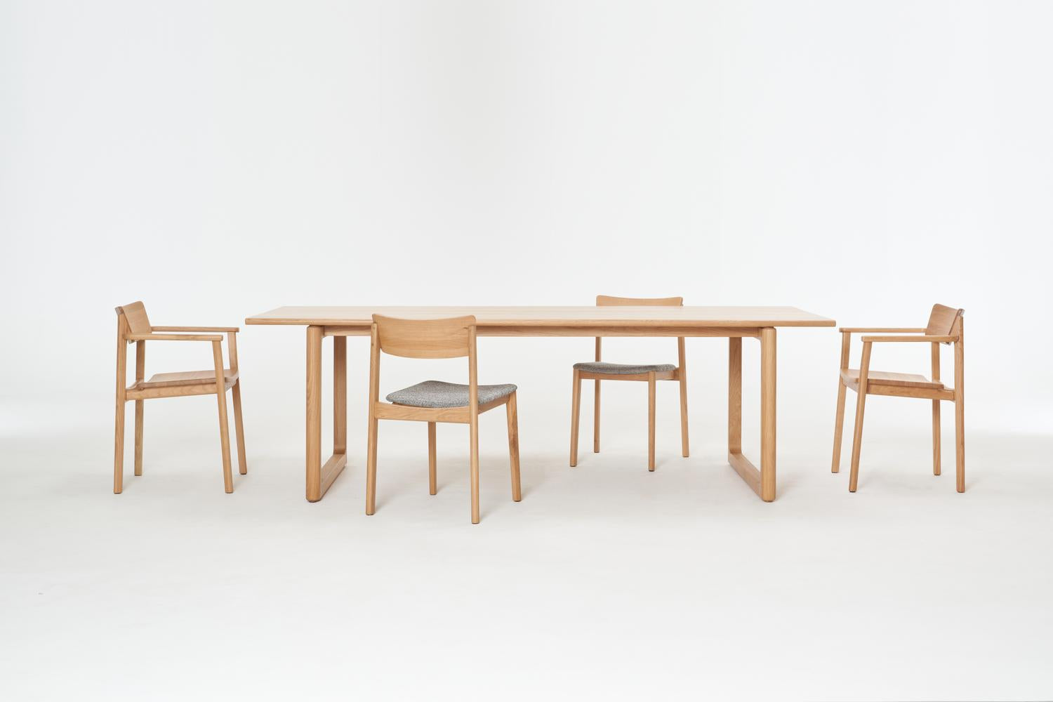 The Wooden Stories Hover Dining Table in Light Oak is paired with four matching chairs featuring grey seat cushions and clean lines, all set against a plain white background—an ideal minimalist touch for any modern dining room.