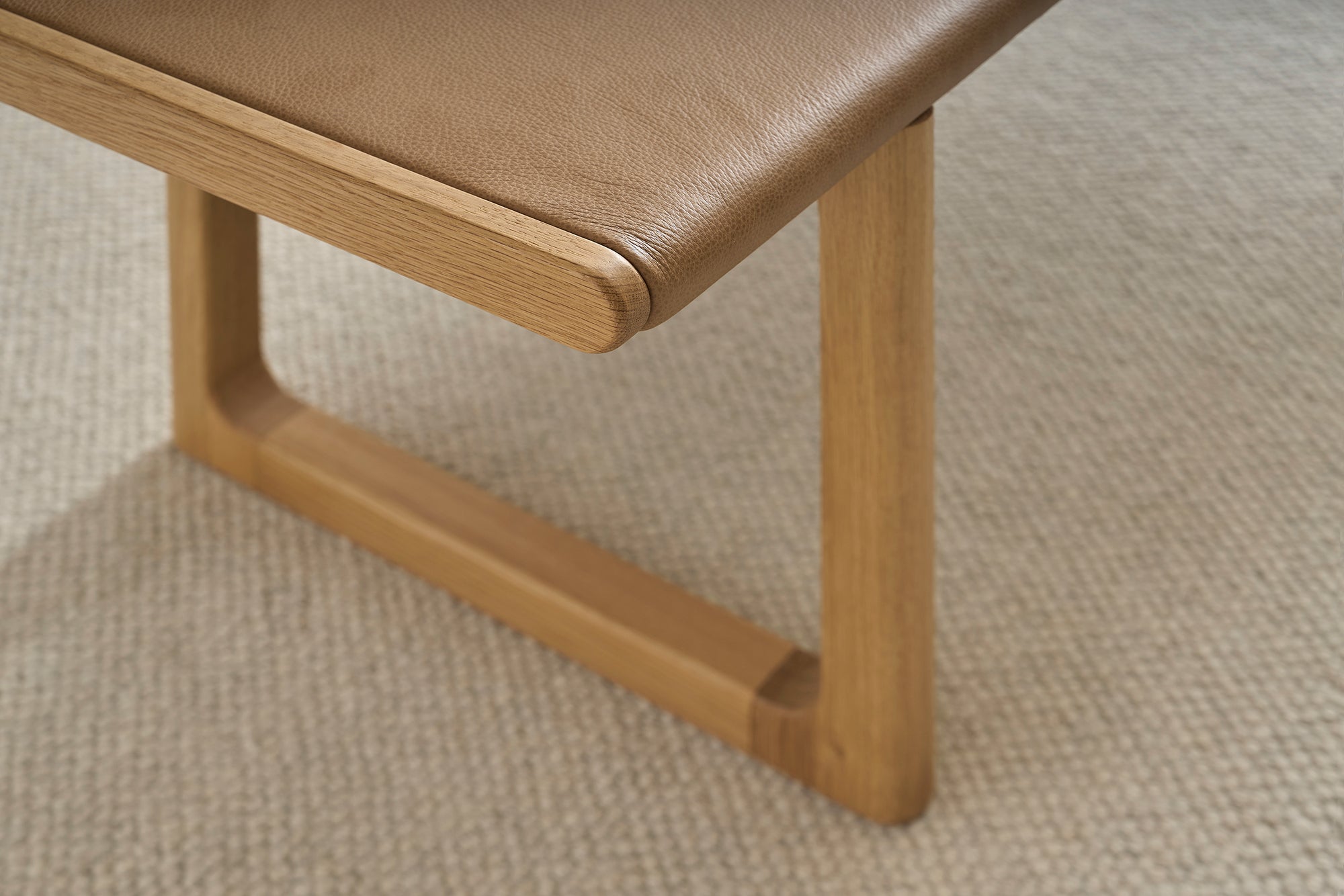 Close-up of the Hover Bench | Leather Seat by Wooden Stories, featuring a solid oak frame with smooth edges and brown leather seat, set on a light textured carpet. Its modern Scandinavian design combines minimalism and elegance.