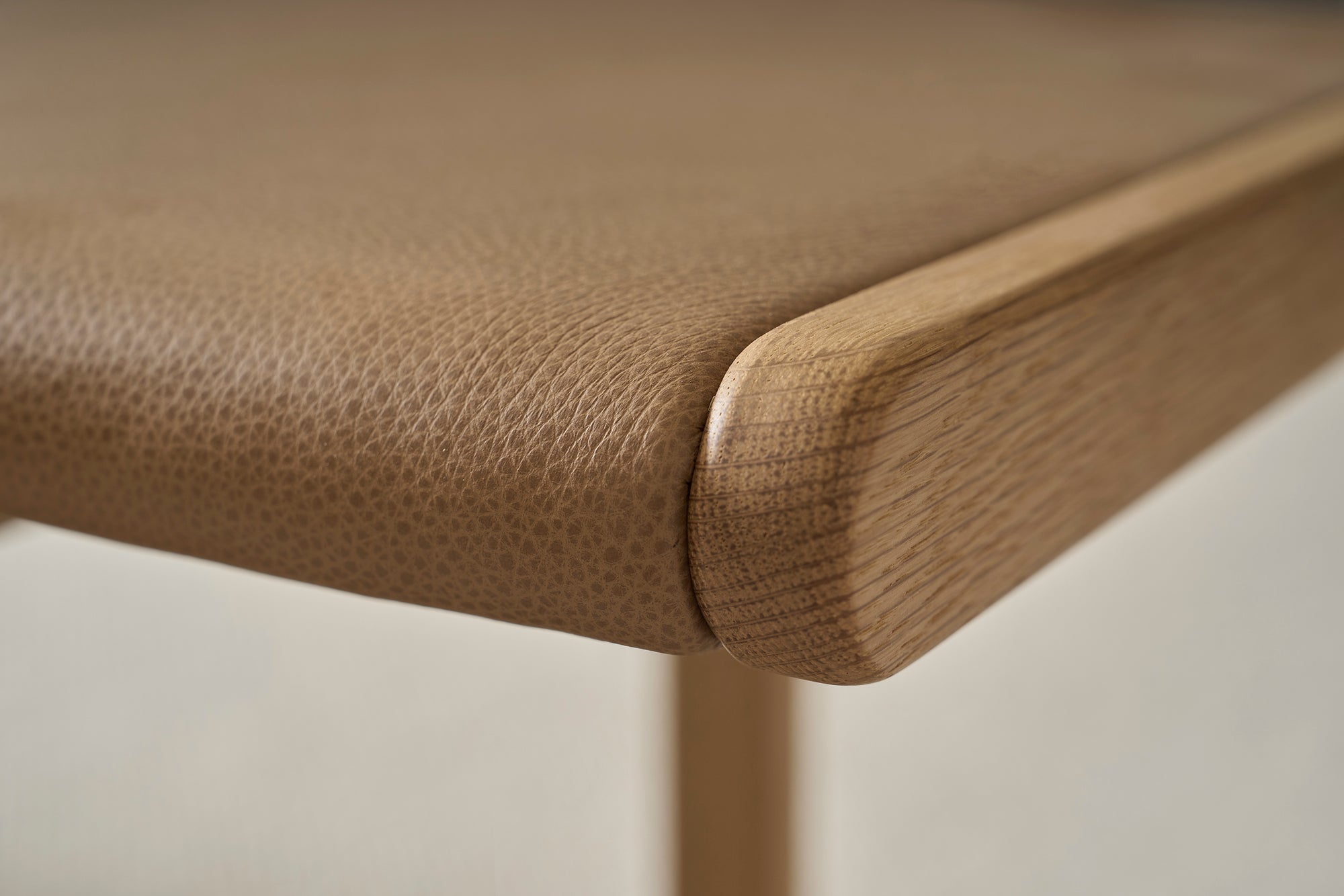 Close-up of Wooden Stories' Hover Bench | Leather Seat: solid oak corner with textured tan leather top, highlighting fine grain and smooth rounded edges—ideal for contract grade furniture settings.