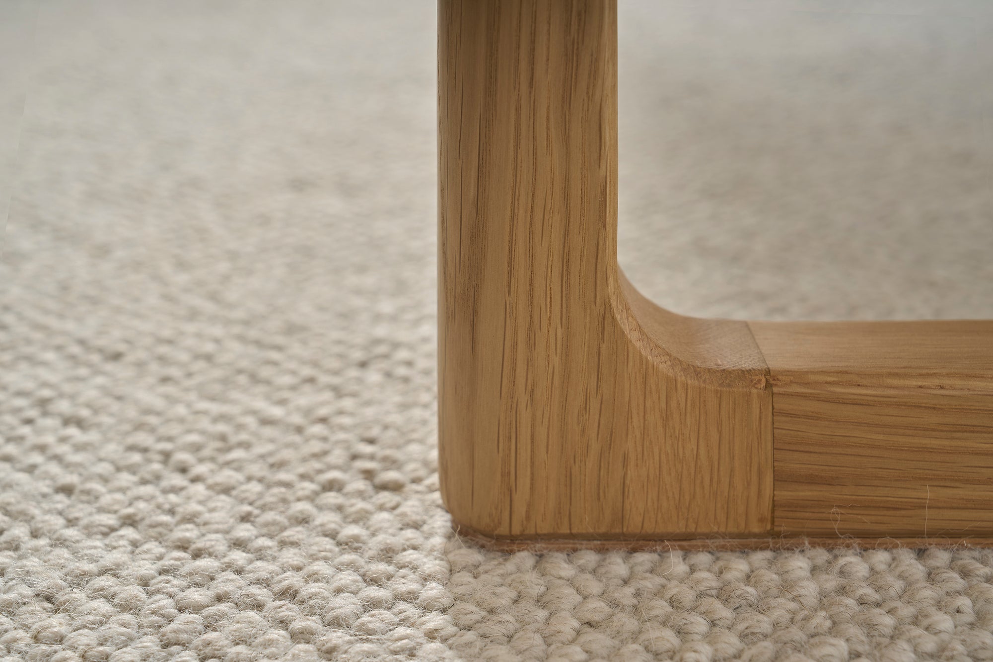 Close-up of a Hover Bench | Leather Seat by Wooden Stories shows its solid oak leg with smooth corners on a textured light carpet, highlighting the wood grain and joints that reflect its contract grade quality.