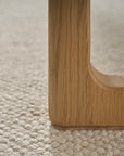 Close-up of a Hover Bench | Leather Seat by Wooden Stories shows its solid oak leg with smooth corners on a textured light carpet, highlighting the wood grain and joints that reflect its contract grade quality.