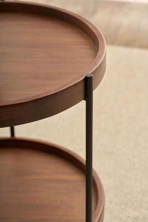 Close-up of the Humla Round Side Table by Wooden Stories, a Danish-inspired design with a raised edge, metal legs, and two shelves, shown on a light-colored textured rug—evoking classic Hans Bolling tray tables.
