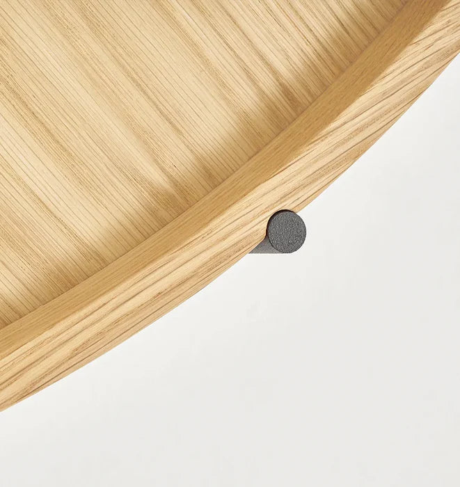 Close-up of the Humla Round Side Table by Wooden Stories, featuring light wood grain and Danish-inspired design. A black cylindrical metal support beneath the rim recalls classic Tray Tables, set against a plain white background.