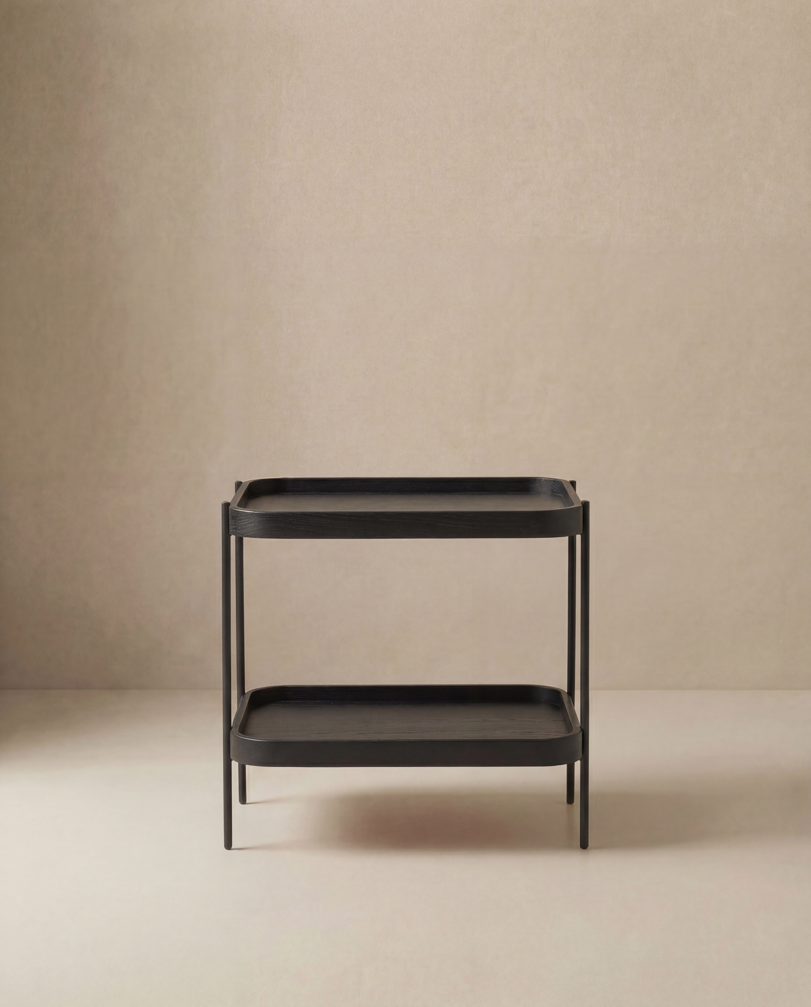 The Wooden Stories Humla Rectangular Side Table, a minimalist black piece with two shelves, features clean lines and modern Danish design inspired by Hans Bolling tray tables, shown against a plain beige background.