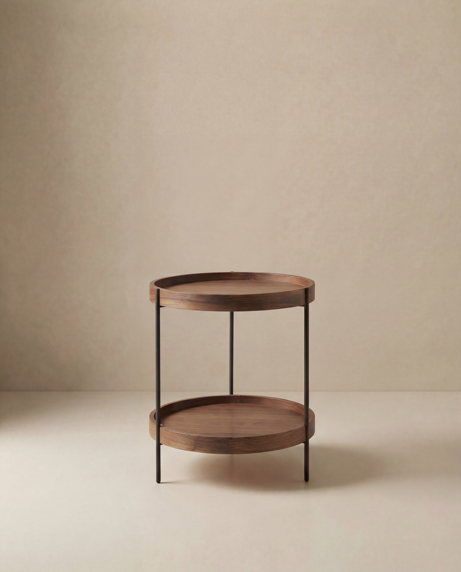 The Humla Round Side Table by Wooden Stories is a Danish-inspired wooden piece with two shelves and slim black metal legs, echoing Hans Bolling’s Tray Tables, shown on a plain beige background.