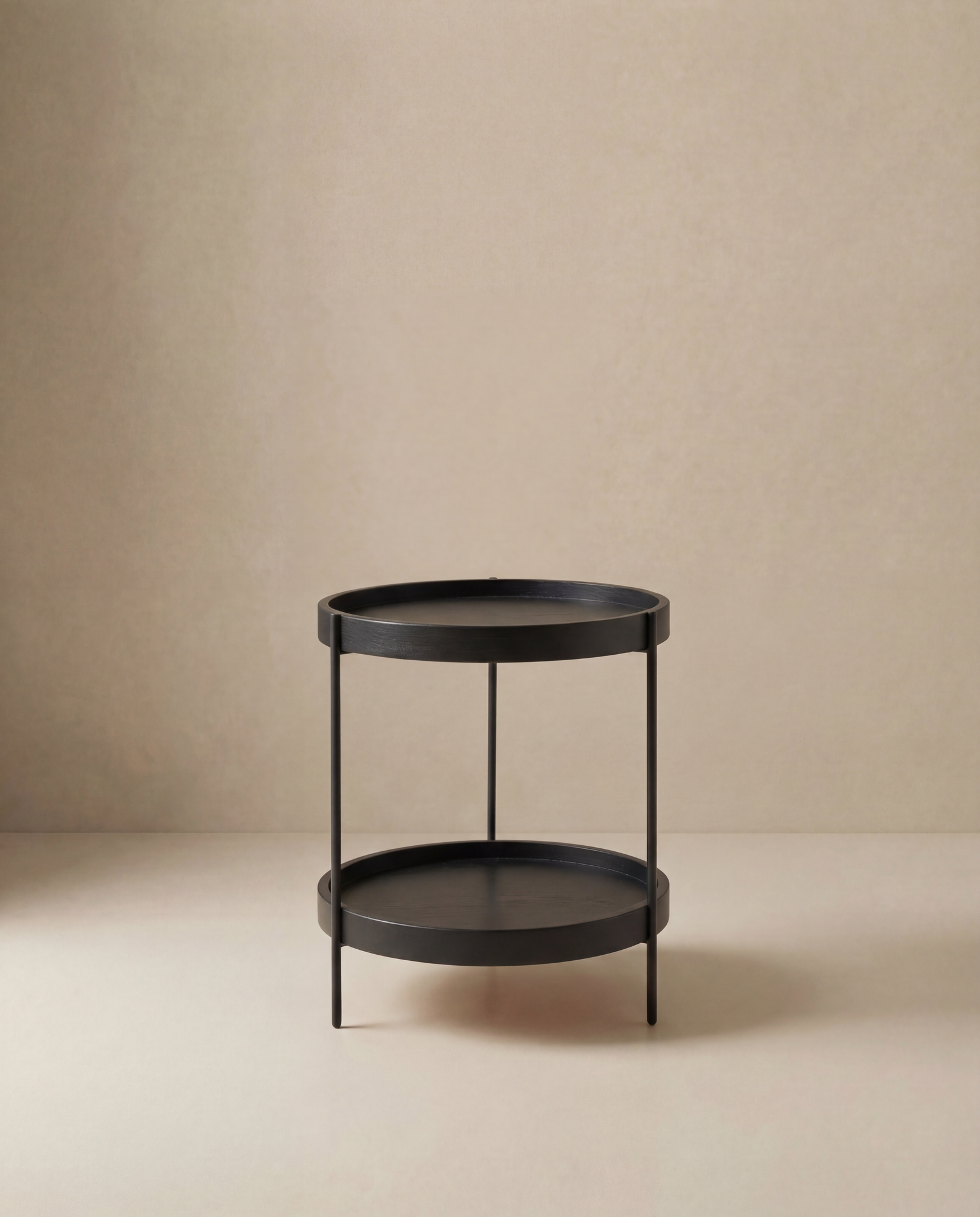 The Wooden Stories Humla Round Side Table features a minimalist black metal design with two tiers and four slender legs, exemplifying refined Danish style against a plain beige background.