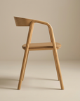 The Wooden Stories Inlay Dining Chair | Light Oak and Leather features a curved backrest, minimalist design, smooth rounded edges, and a light solid oak finish, set against a neutral beige background.