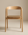 The Wooden Stories Inlay Dining Chair | Light Oak and Leather features curved armrests and a light brown cushioned seat, set on a neutral floor with a beige background.