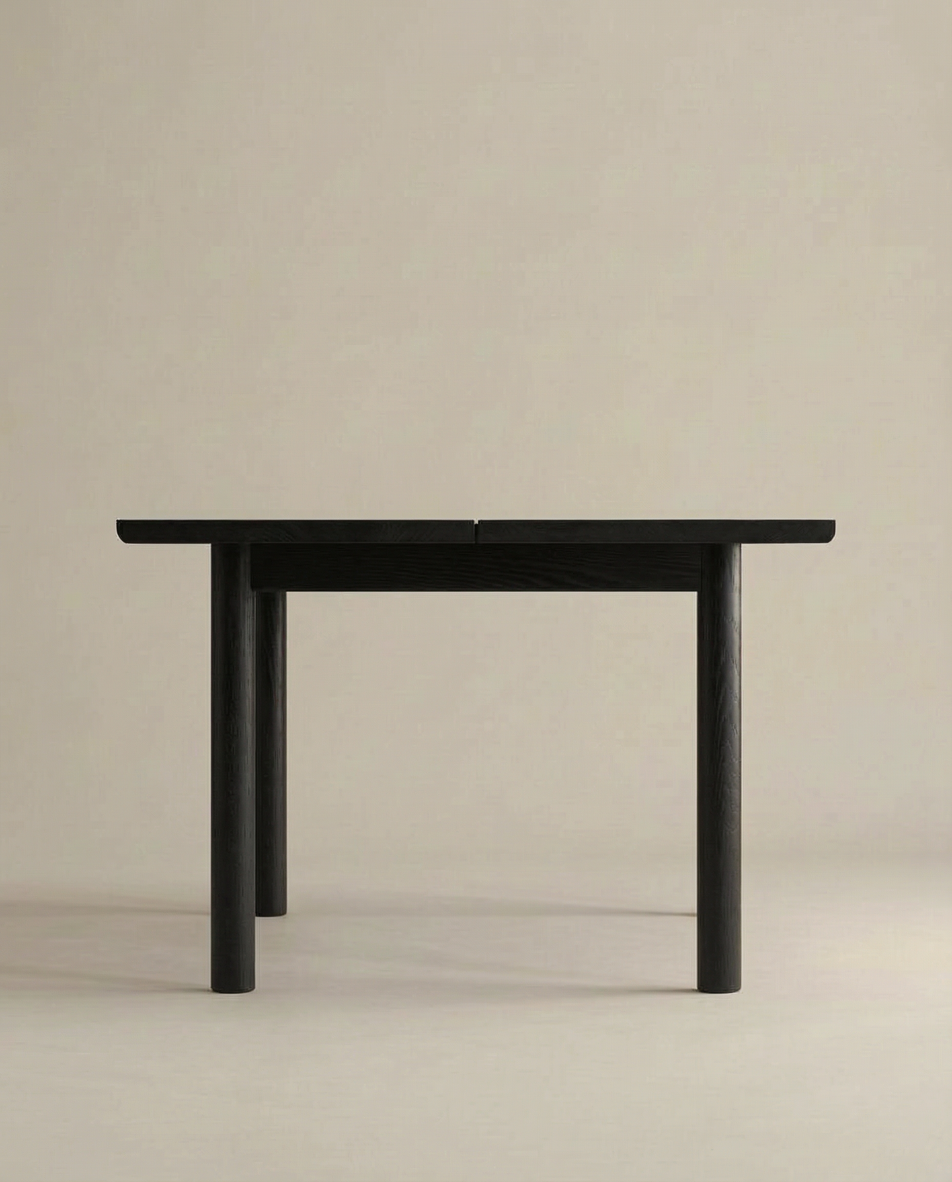The Wooden Stories Itamae Dining Table | Black Oak features a minimalist Scandinavian-inspired design with four thick cylindrical legs, showcased against a plain beige background.