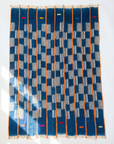 The Indigo Horizon — Vintage Baule Cloth Throw by Riad Jardin Des Biehn is a handwoven cotton textile featuring vertical orange stripes, blue and gray checkered patterns, and green, red, and yellow bars on an indigo background.