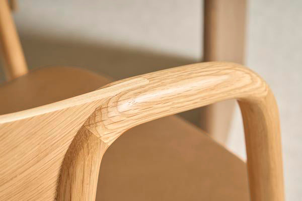 Close-up of the Inlay Dining Chair | Light Oak and Leather by Wooden Stories, highlighting the curved solid oak armrest, leather seat, and natural wood grain. The craftsmanship stands out against a softly blurred background.