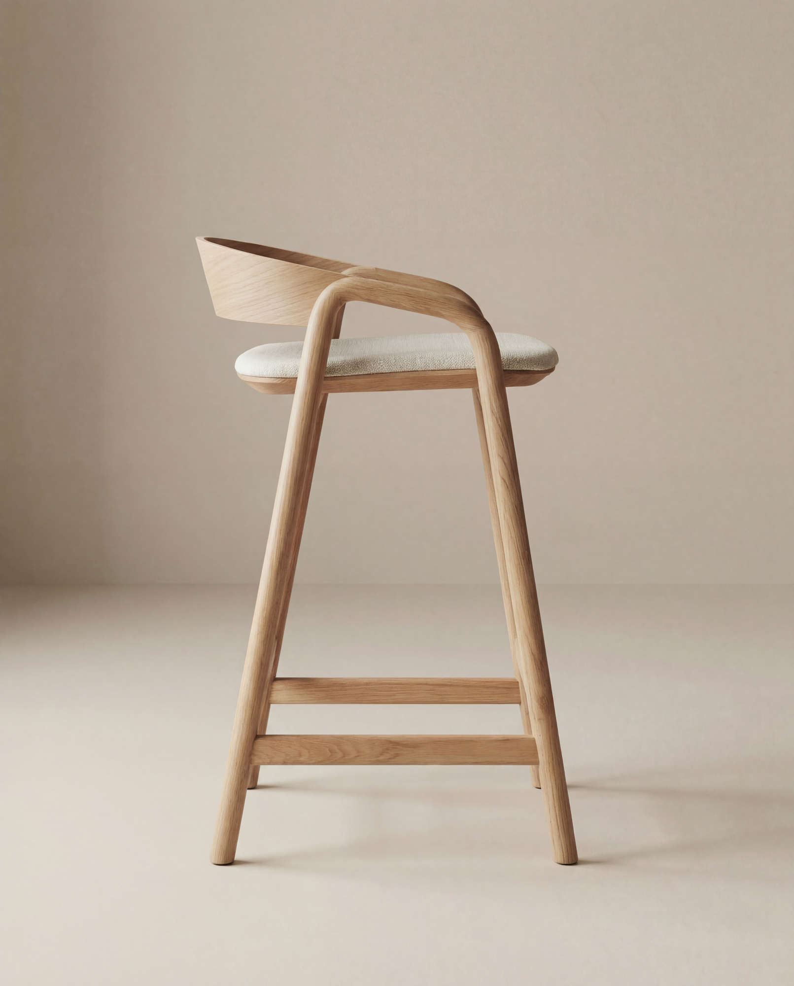 The Inlay Counter Stool by Wooden Stories features a modern solid oak frame, light wood legs, a curved low backrest, and a cushioned light beige fabric seat, set in a minimalistic environment.