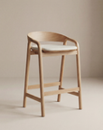 The Inlay Counter Stool | Fabric Seat from Wooden Stories features a modern design with a solid oak frame, curved backrest, and a light fabric-cushioned seat, showcased against a plain beige background.