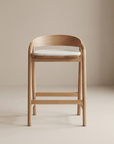 The Inlay Counter Stool | Fabric Seat by Wooden Stories features solid oak, a curved backrest, and a light fabric seat, styled against a neutral beige background.
