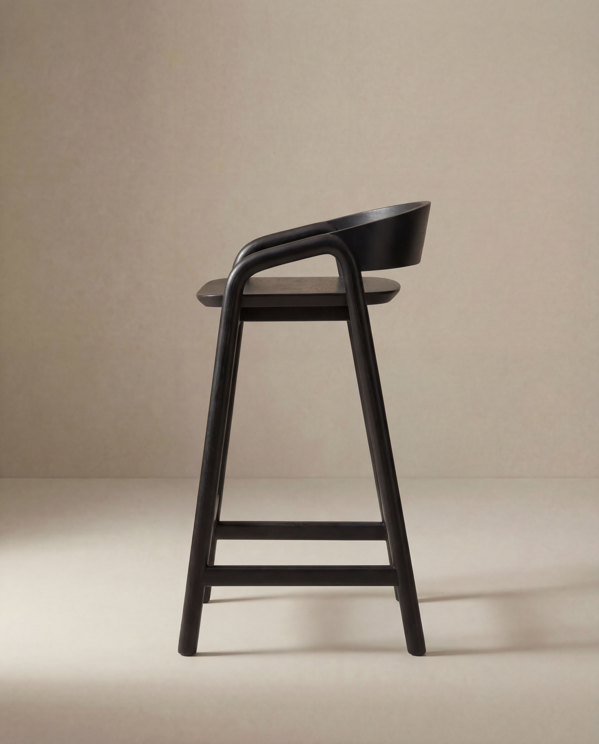 The Inlay Counter Stool | Wood Seat by Wooden Stories features a modern black solid oak design with a curved backrest and footrest, shown in profile against a beige background.