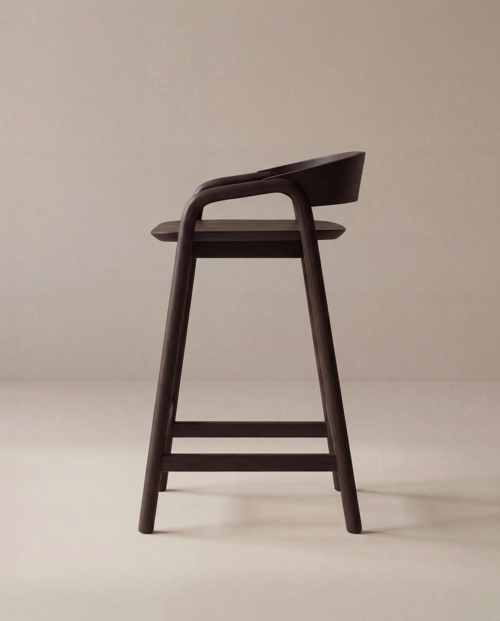 The Inlay Counter Stool | Wood Seat by Wooden Stories, featuring a modern dark wood design with a curved seat and backrest, is shown sideways against a beige background—ideal for stylish kitchen island seating.