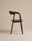 Side view of the Inlay Dining Chair | Wood by Wooden Stories, featuring a minimalist, modern solid oak design from the Danish Collection with a curved backrest and seat, set against a plain beige background. The chair’s sleek silhouette highlights its smooth finish and elegant lines.