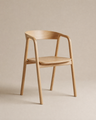 The Wooden Stories Inlay Dining Chair | Wood features a light oak frame with a curved backrest and armrests, showcased against a beige background. Its minimalist, modern design—marked by smooth, clean lines—captures the essence of the Danish Collection aesthetic. Combining elegance and durability, this solid oak dining chair by Wooden Stories offers timeless appeal for any dining space.