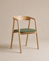 An Inlay Dining Chair | Fabric by Wooden Stories, crafted in solid oak with armrests, a curved backrest, and a green cushioned seat, is placed against a neutral beige background.