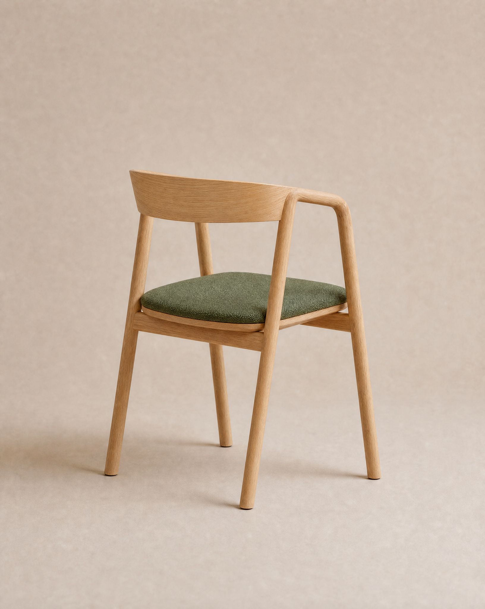 A modern solid oak wooden chair with a curved backrest and green upholstered seat, positioned at an angle against a neutral beige background, from Wooden Stories’ Inlay Dining Chair | Fabric collection.