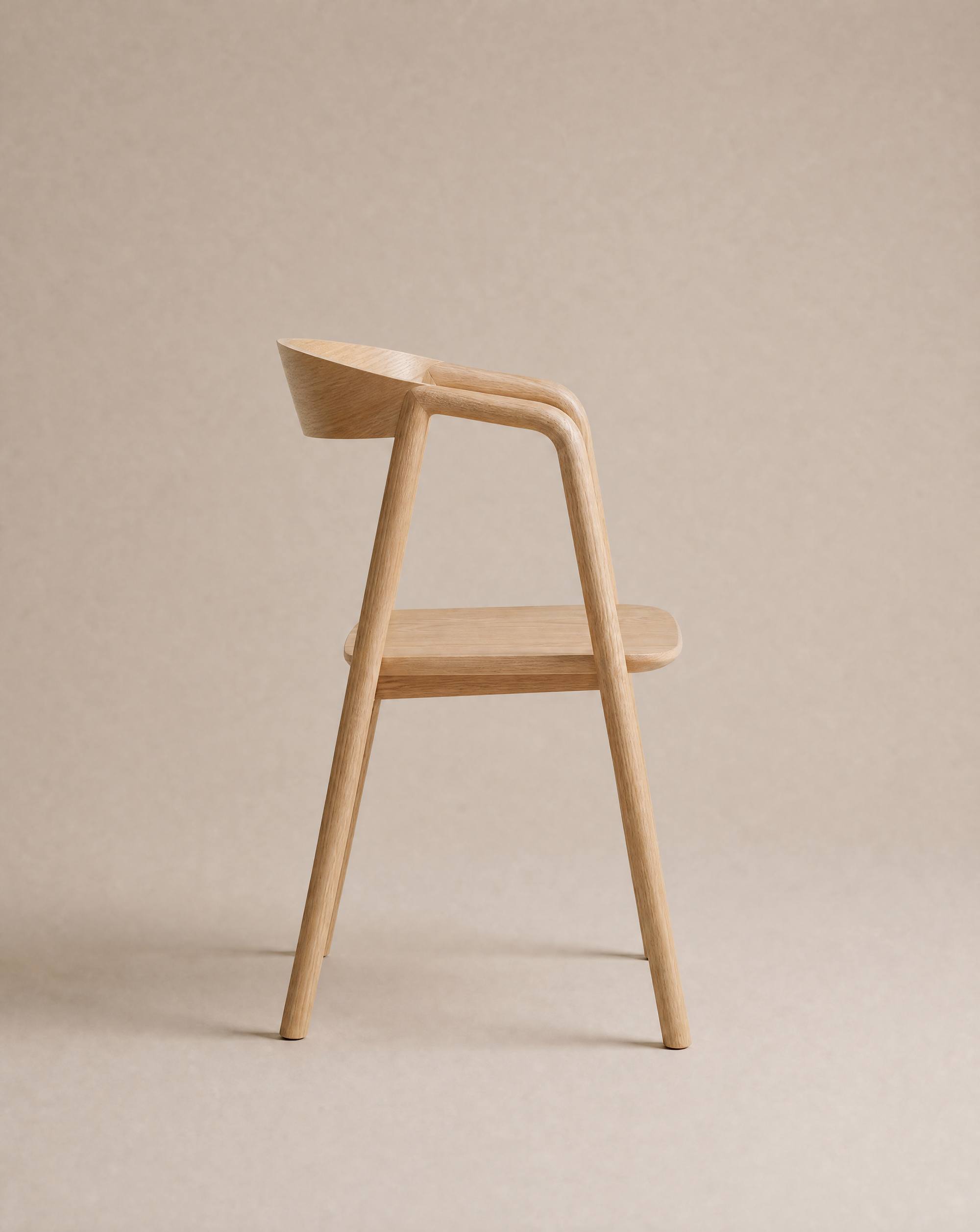 A minimalist wooden chair with smooth curves is shown in profile against a neutral beige background. The Inlay Dining Chair | Wood from Wooden Stories features a light wood finish, seamlessly blending form and function to suit contemporary interiors.