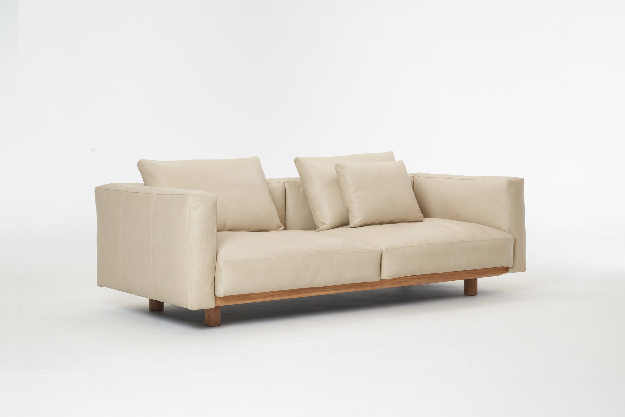 The Islet Sofa | Leather by Wooden Stories is a modern beige sofa with durable leather upholstery, wooden legs, two large seat cushions, and three matching back cushions, shown against a plain white background.